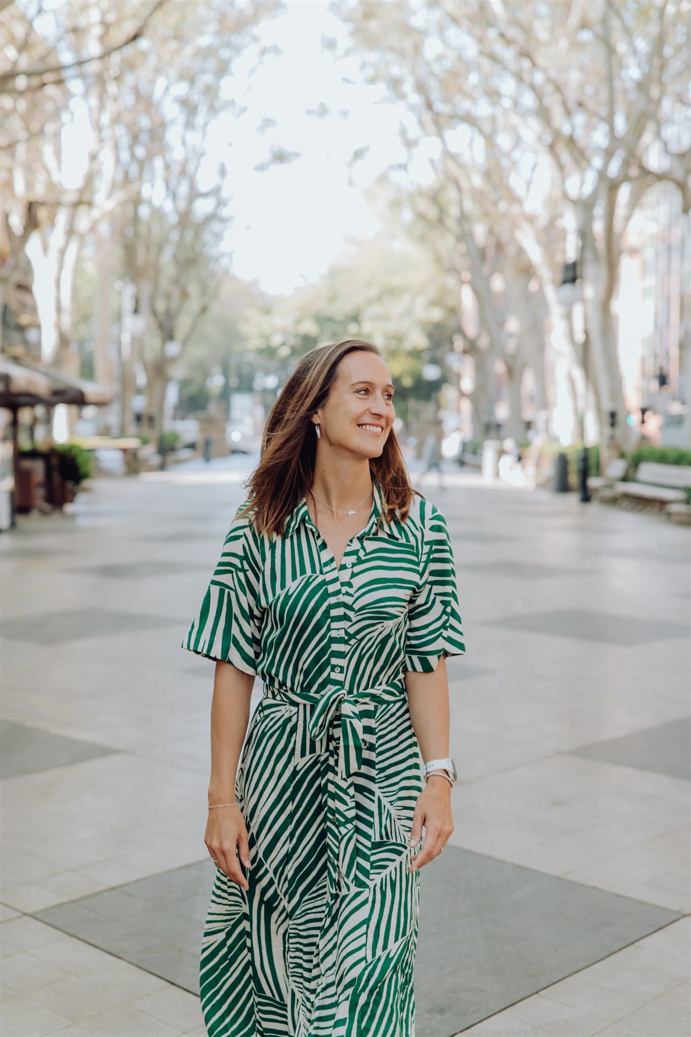Sofie in a green and white striped dress standing on a tree-lined pathway