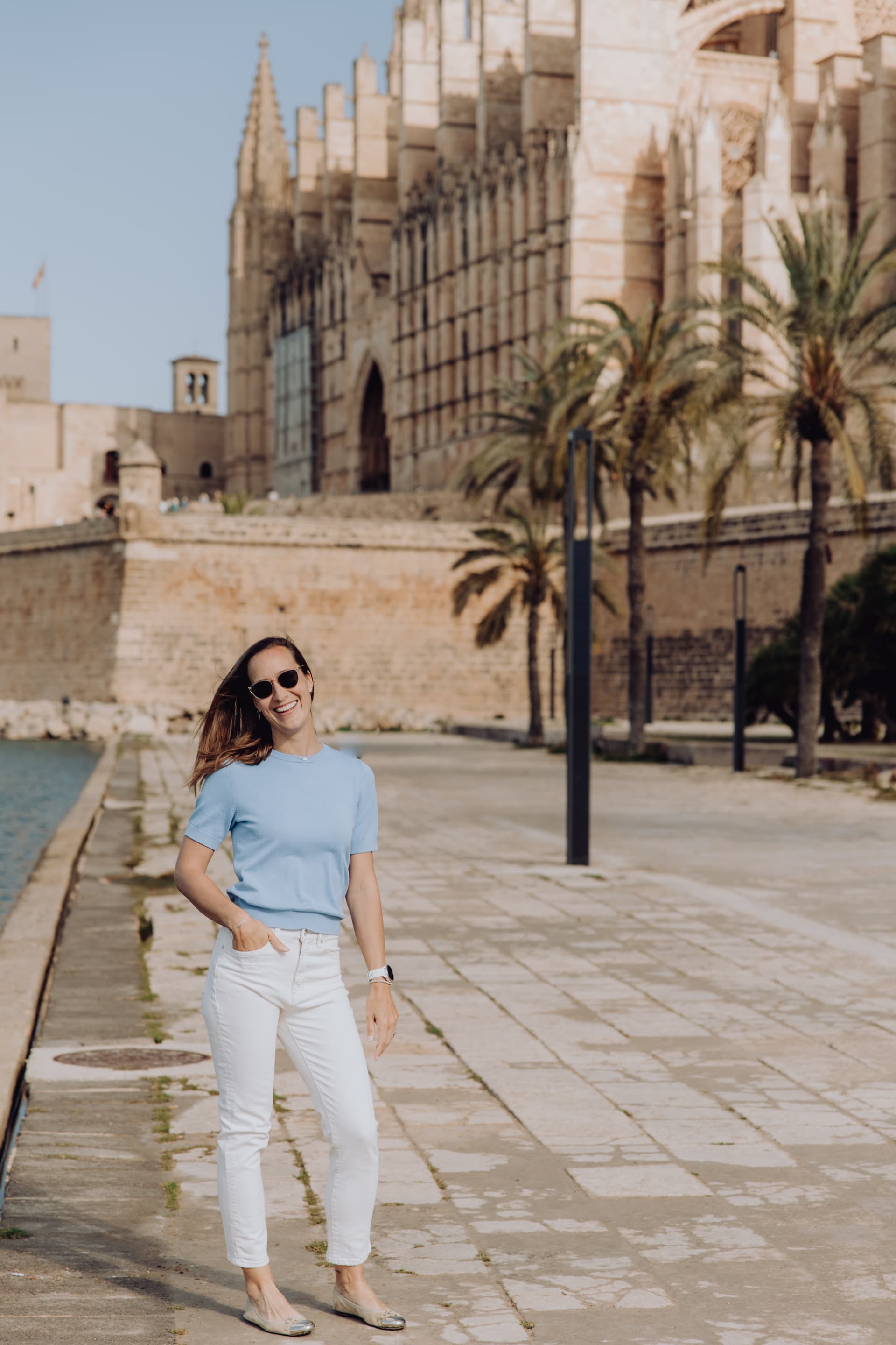 Sofie smiling in front of Palma Cathedral in Mallorca, wearing a light blue top and white pants